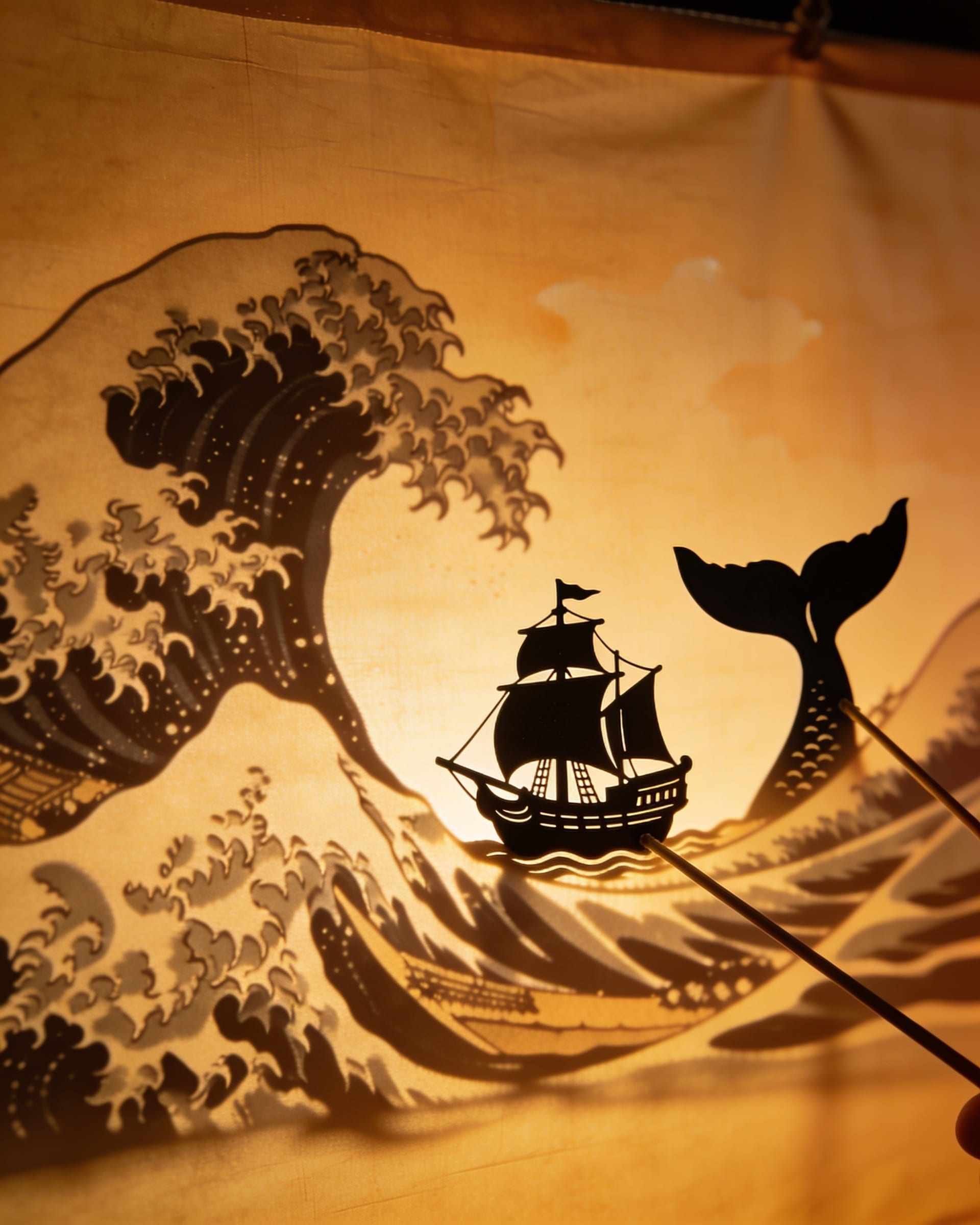 A shadow scene on a glowing screen: a sailing ship on tall waves with a whale’s tail rising beside it